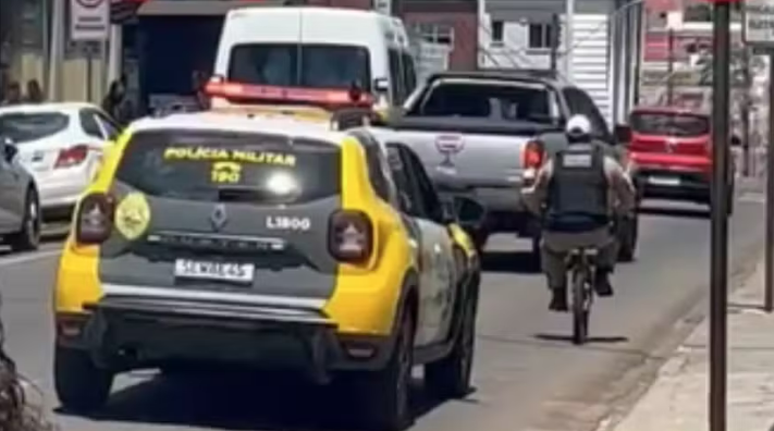  Policial Militar leva ‘mini’ bicicleta apreendida para delegacia pedalando pela rua, ao lado de viatura